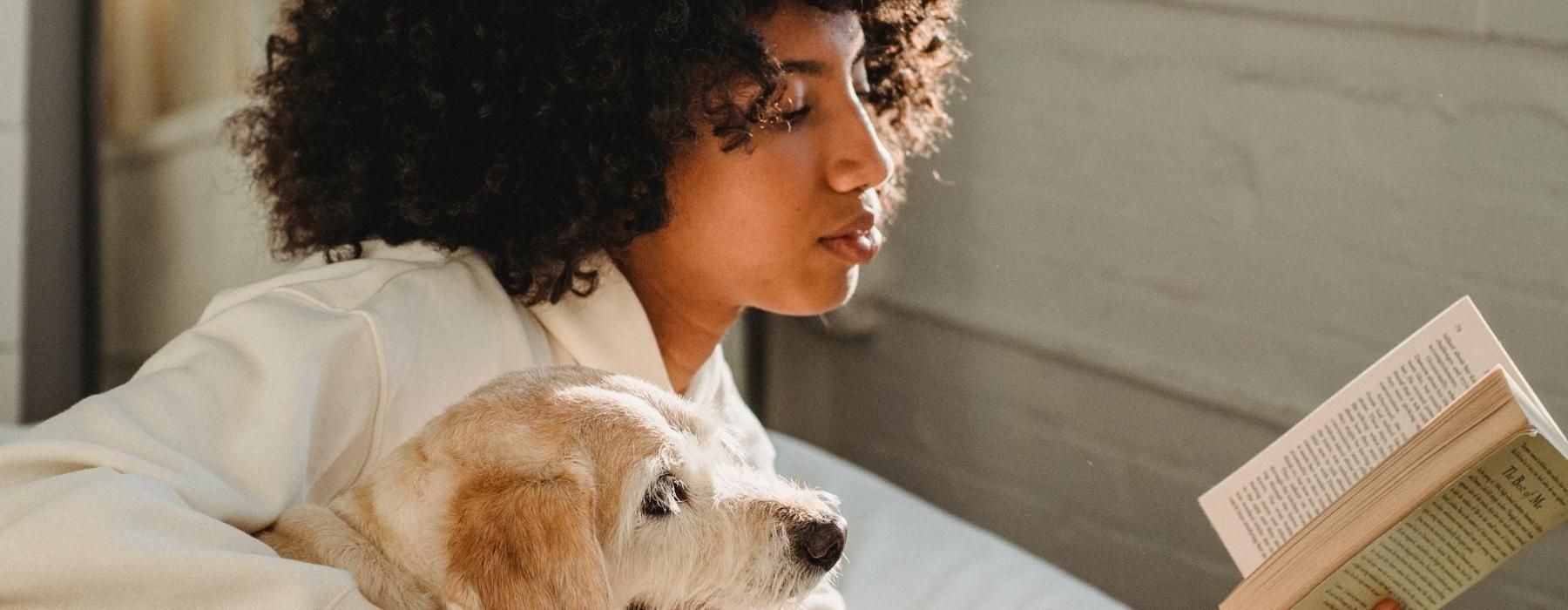 a person reading a book while laying next to a dog